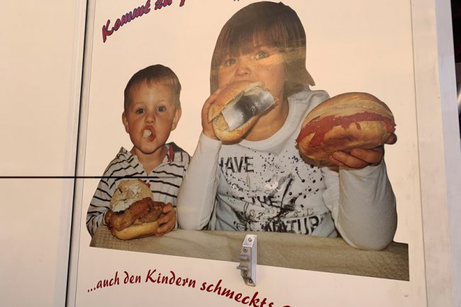 Fahrzeugbeschriftung zeigt Foto, wie zwei Kinder in Fischbrötchen beißen. Die Darstellung ist bizarr, das Foto wirk amateurhaft.