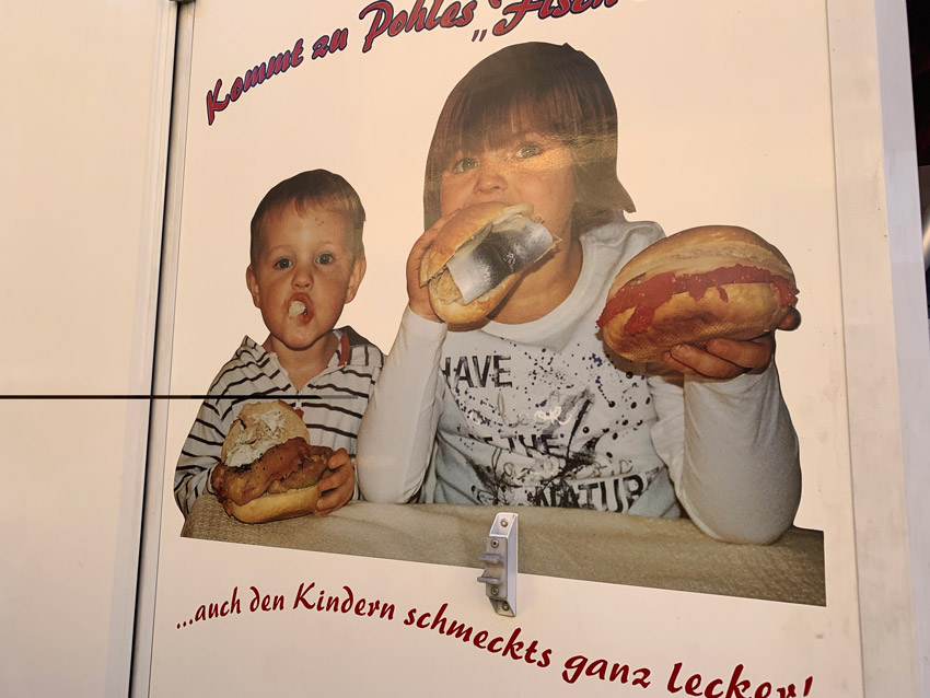 Fahrzeugbeschriftung zeigt Foto, wie zwei Kinder in Fischbrötchen beißen. Die Darstellung ist bizarr, das Foto wirk amateurhaft.