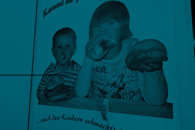 Fahrzeugbeschriftung zeigt Foto, wie zwei Kinder in Fischbrötchen beißen. Die Darstellung ist bizarr, das Foto wirk amateurhaft.